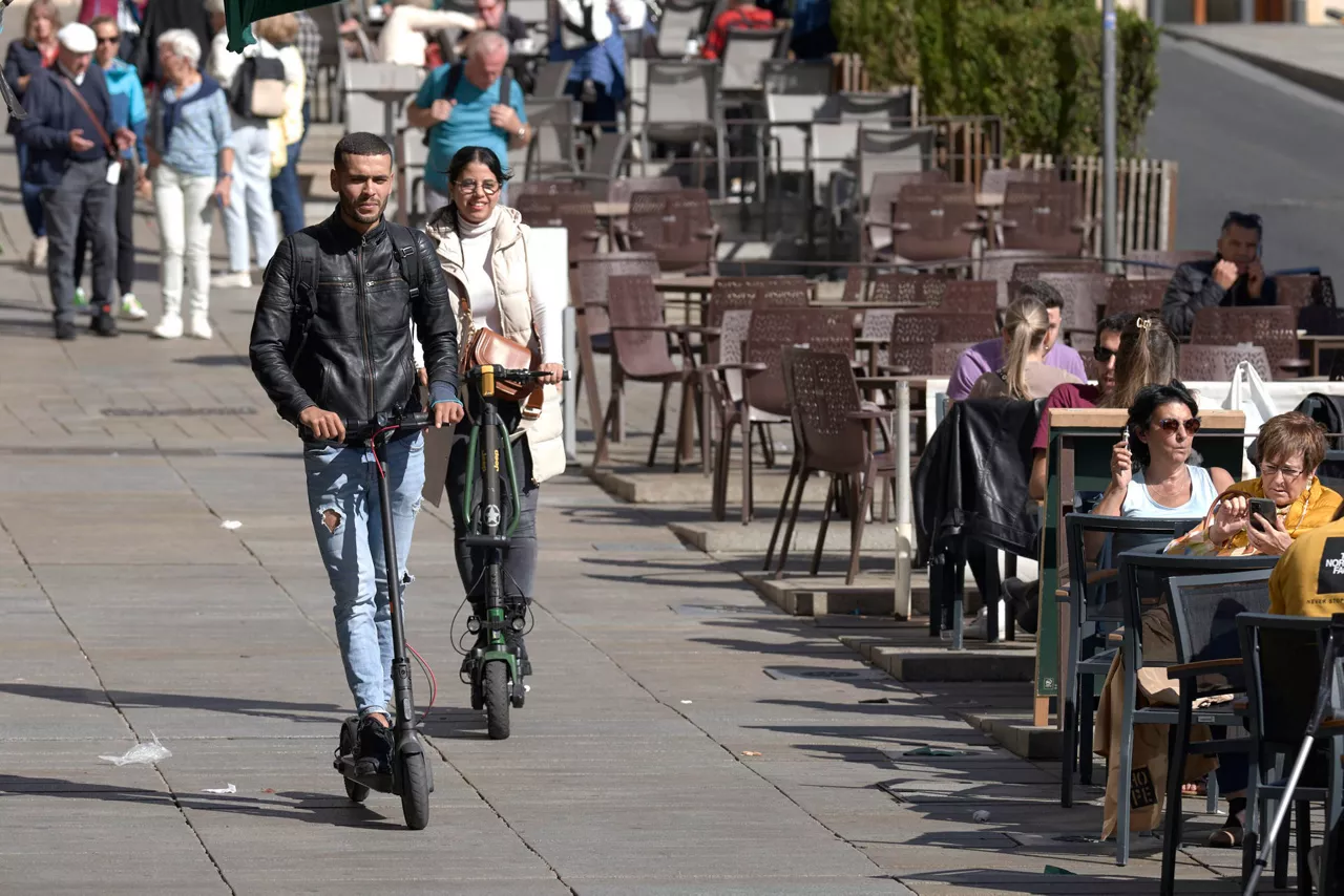 VITORIA, 18/10/2023.-El Ayuntamiento de Vitoria modificará de forma urgente la ordenanza municipal de movilidad para prohibir el uso de patinetes eléctricos en aceras y establecer la obligación de que circulen por la calzada o el bicicarril. En la imagen dos personas circulan con dos patinetes eléctricos por una acera llena de terrazas del centro de Vitoria. EFE/ADRIAN RUIZ HIERRO
