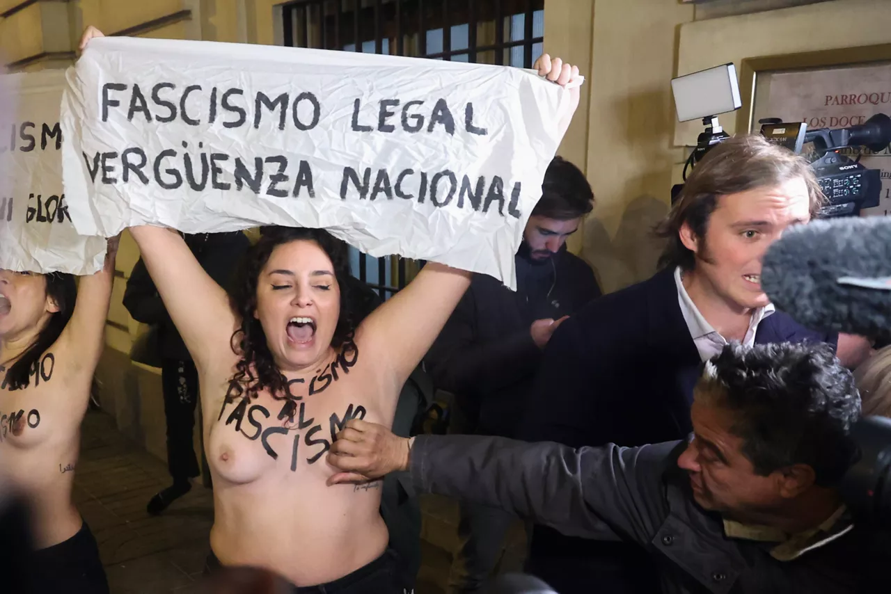 Un hombre toca el pecho a una de los dos activistas de Femen que protestan semidesnudas con motivo de la misa organizada por la Fundación Francisco Franco en recuerdo al dictador y a la que asiste la familia, este jueves en la parroquia de los Doce Apóstoles, en la calle Velázquez en Madrid.