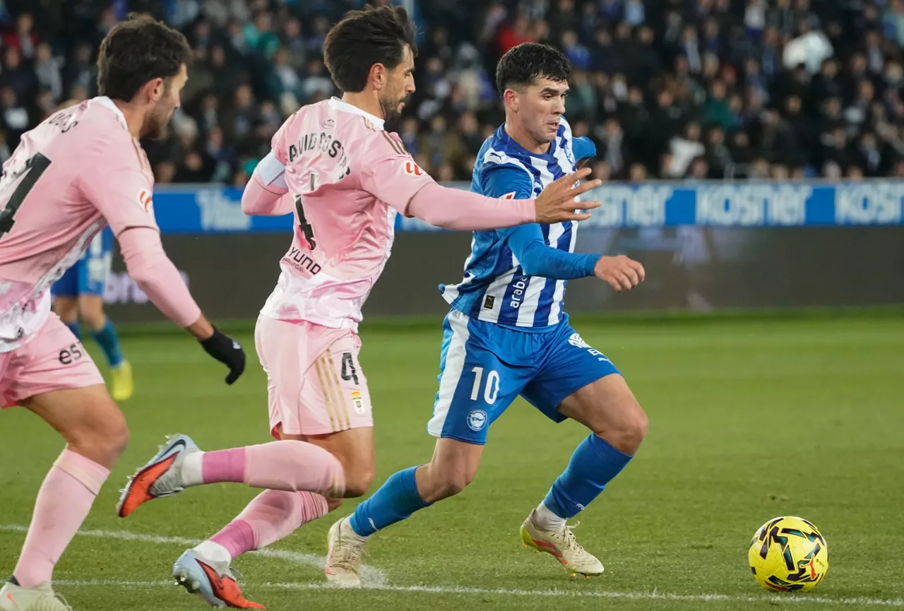 VITORIA, 04/01/2026.- El centrocampista del Alavés Carlos Aleñá (d) controla el balón ante dos rivales del Oviedo en el partido de LaLiga que se disputa este domingo en el estadio de Mendizorroza. EFE / L. Rico
