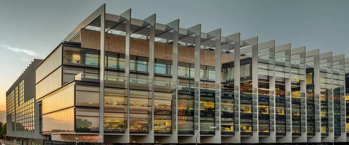 Vista del Campus Repsol desde la calle de enfrente donde se ve la fachada y la entrada del garaje iluminado con la luz del sol anocheciendo