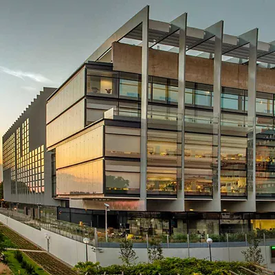 Vista del Campus Repsol desde la calle de enfrente donde se ve la fachada y la entrada del garaje iluminado con la luz del sol anocheciendo