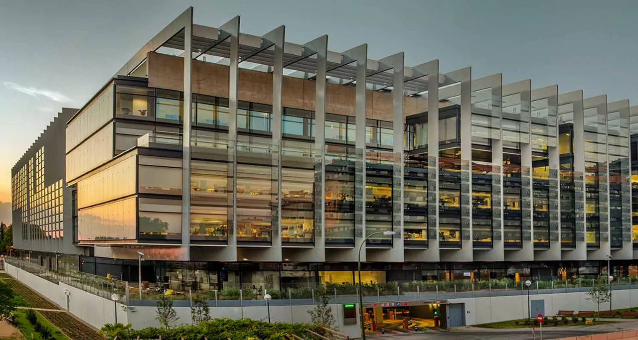 Vista del Campus Repsol desde la calle de enfrente donde se ve la fachada y la entrada del garaje iluminado con la luz del sol anocheciendo