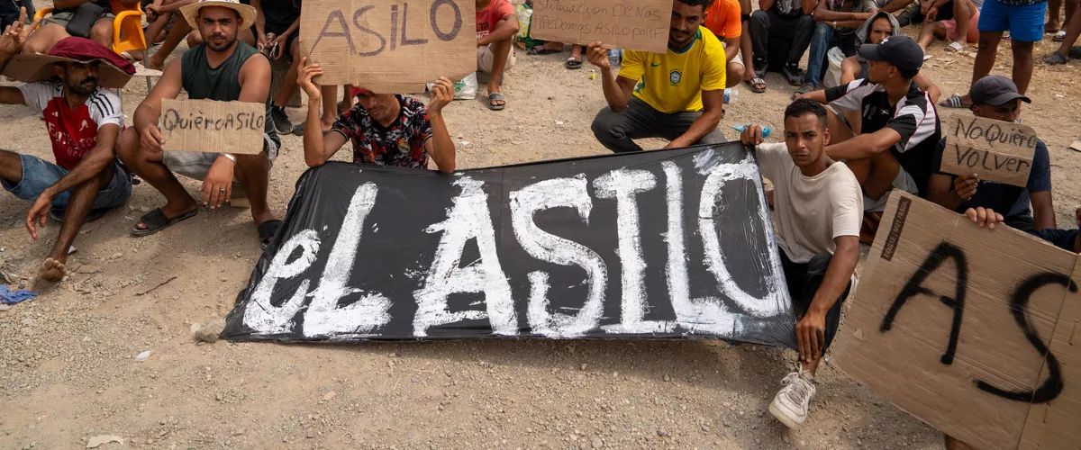 CEUTA (ESPAÑA), 16/08/2026.- Un grupo de migrantes concentrados para solicitar asilo este domingo en la playa del trampolín de Ceuta. EFE/ Reduan
