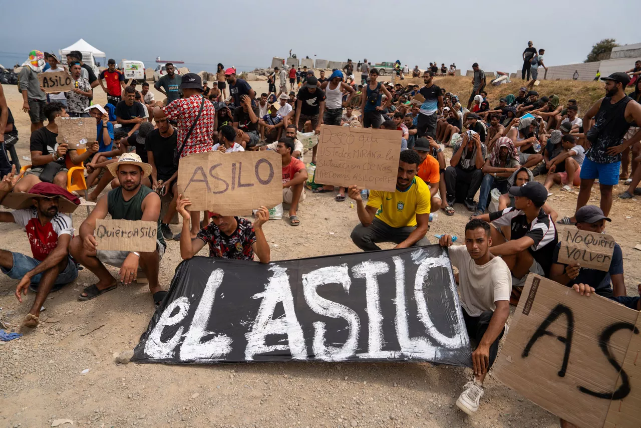 CEUTA (ESPAÑA), 16/08/2026.- Un grupo de migrantes concentrados para solicitar asilo este domingo en la playa del trampolín de Ceuta. EFE/ Reduan
