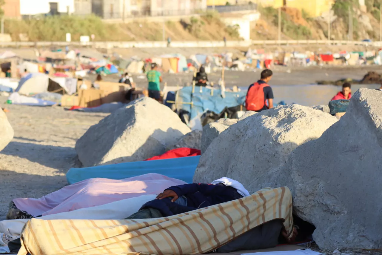 CEUTA, 27/08/2026.- Migrantes acampan en la playa de El Trampolín, en Ceuta, este jueves. La Policía y la Guardia Civil han detenido a doce migrantes por apedrear un vehículo con cuatro militares en una noche de disturbios en Ceuta en la que las fuerzas de seguridad han tenido que disparar salvas al aire para contener a los ceutís que querían atacar a migrantes en las playas del Trampolín y Benítez. EFE/ Reduan
