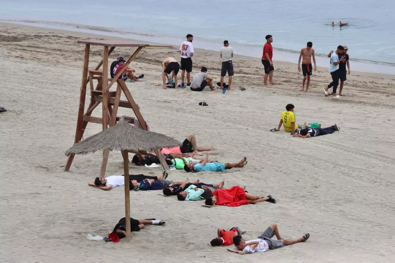 CEUTA (ESPAÑA), 31/07/2026.- Inmigrantes descansan este viernes en una de las playas de Ceuta, donde se han registrado violentos enfrentamientos en los perímetros fronterizos durante su intento de acceder desde Marruecos hacia Ceuta y Melilla. EFE/ Reduan Dris
