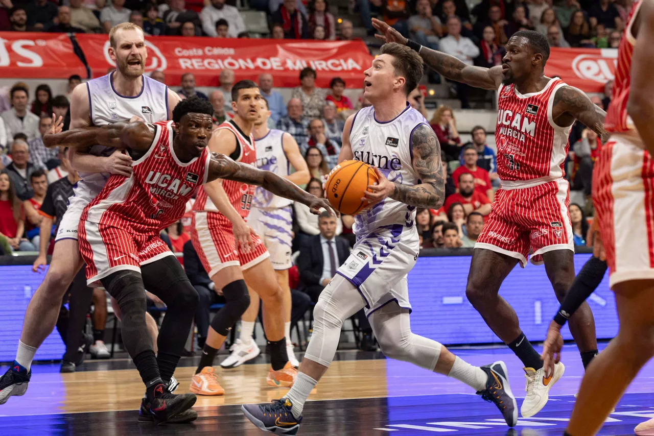 MUR01.MURCIA, 28/03/2026.- El escolta estadounidesne de Surne Bilbao Jaworski (c) controla la pelota ante la presión del base estadounidense de UCAM Murcia Dylan Ennis (d), durante el partido de la vigésima cuarta jornada de la Liga Endesa que están disputando este sábado en el Palacio de los Deportes de Murcia. EFE/Marcial Guillén.
