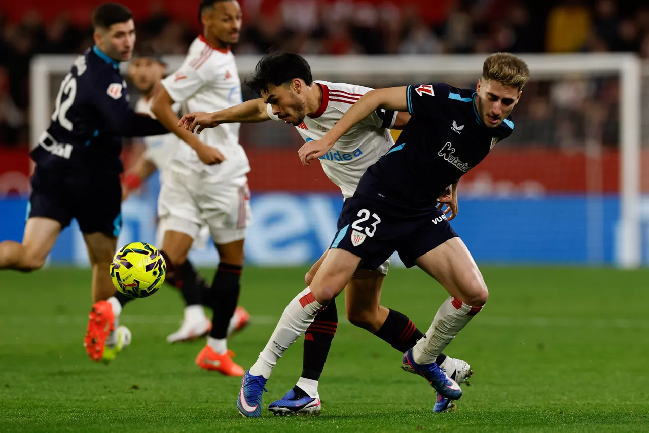 SEVILLA, 24/01/2026.- El delantero del Athletic Club, Robert Navarro (d), disputa el balón ante el defensa chileno del Sevilla, Gabriel Suazo, durante el encuentro correspondiente a la jornada 21 de Laliga EA Sports que disputan hoy sábado Sevilla y Athletic Club en el estadio Sánchez Pizjuán de Sevilla. EFE / Julio Muñoz.
