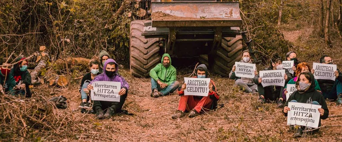 Jóvenes sentados con carteles frente a una excavadora. Foto. Soleil.