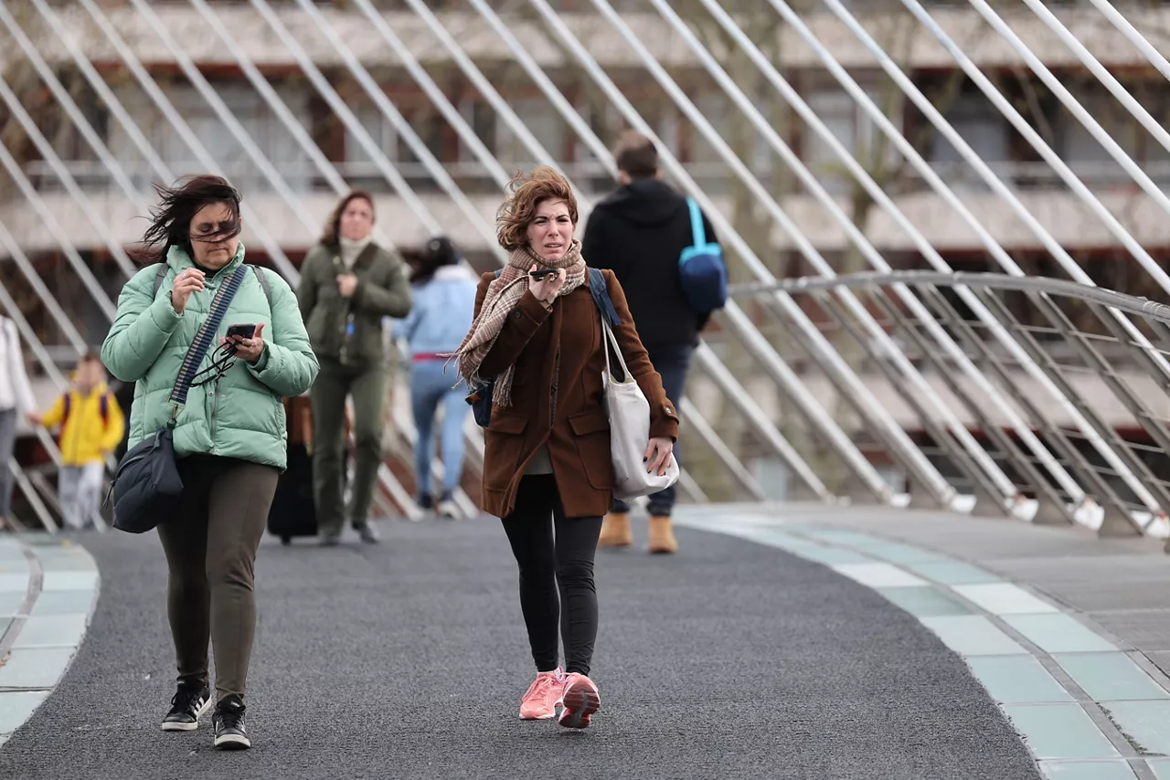 GRAFCAV5012. BILBAO, 20/03/2025.- Peatones cruzan un puente con viento este jueves en Bilbao. Las fuertes rachas de viento que se están registrando en numerosos puntos de Euskadi este jueves han llegado a los 133 kilómetros por hora en el monte Zaldiaran, en Vitoria, y en Matxitxako (Bizkaia), según los datos de la Agencia Vasca de Meteorología-Euskalmet. EFE/Luis Tejido
