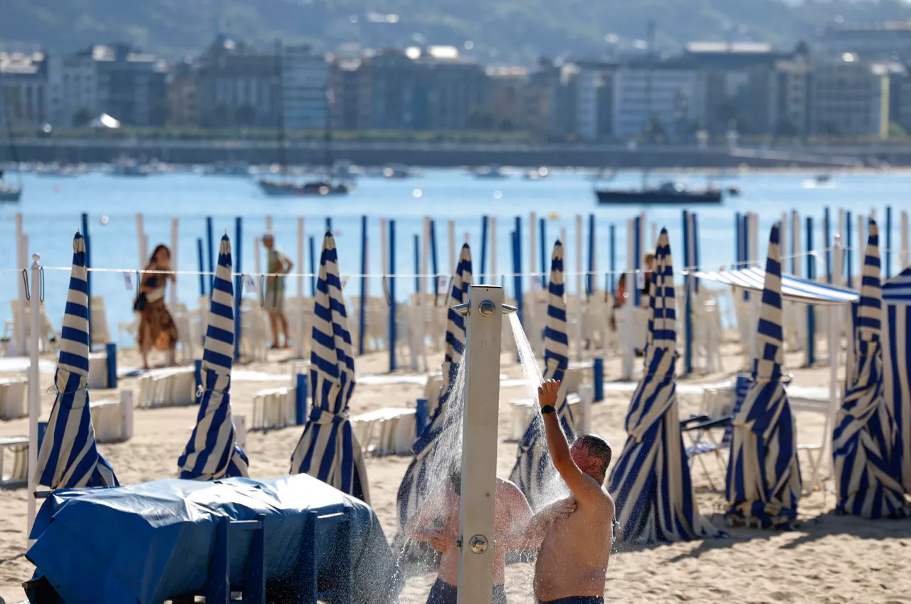 GRAFCAV5822. SAN SEBASTIÁN (ESPAÑA), 06/07/2026.- Unos bañistas se duchan en la playa de Ondarreta de San Sebastián. El Departamento de Seguridad ha activado para este lunes y martes una alerta naranja por temperaturas altas extremas en la totalidad de Euskadi, salvo en la costa donde se espera menos calor y el aviso es amarillo. EFE/Juan Herrero.
