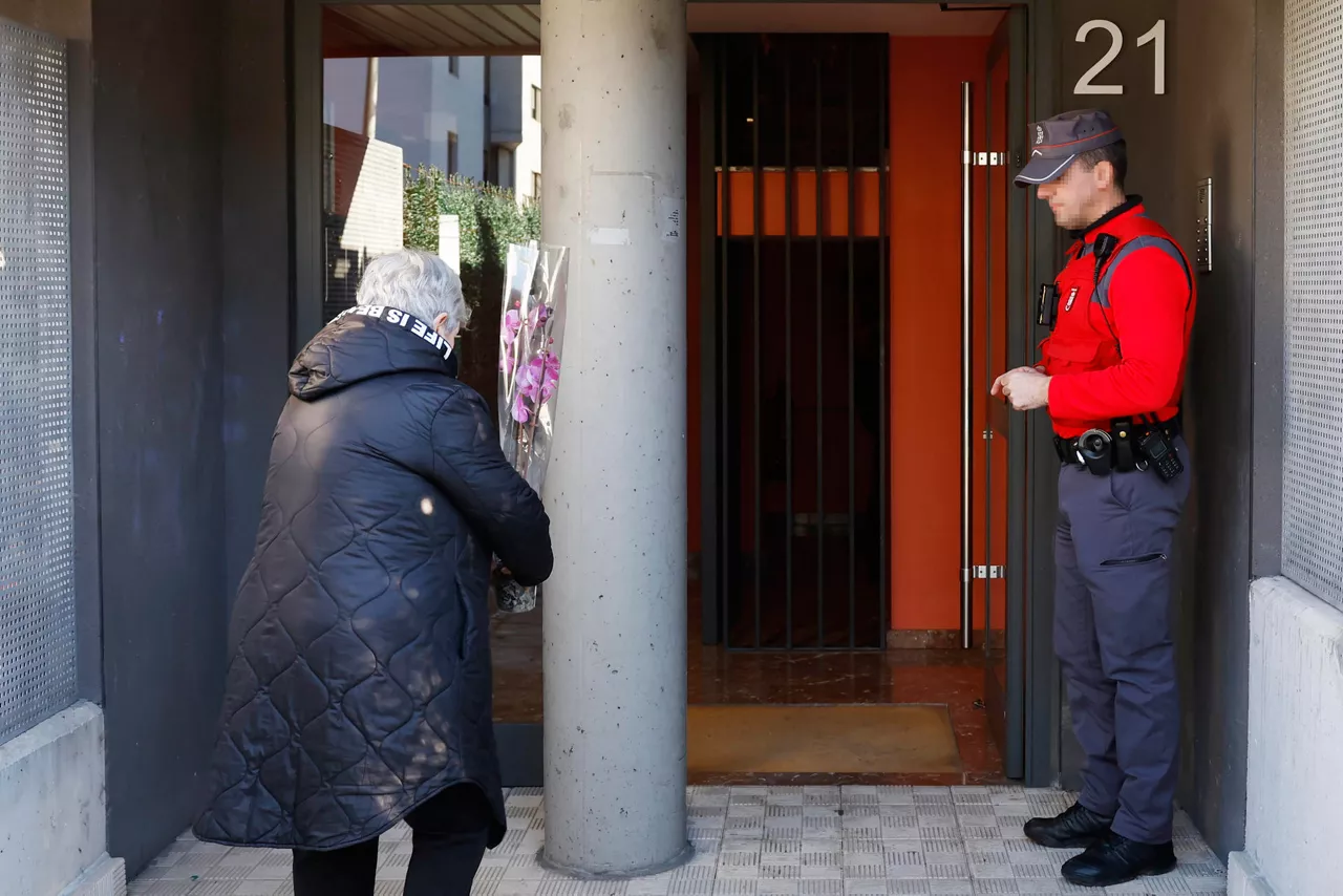 SARRIGUREN, 21/02/2026.- Una mujer deja una planta en el portal de la vivienda de Sarriguren donde dos mujeres fueron víctimas, una de ellas asesinada presuntamente por su marido, en un caso de violencia machista y la otra herida de gravedad. El Ayuntamiento del Valle de Egüés ha decretado tres días de luto oficial. EFE/ Jesús Diges
