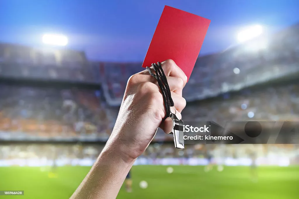 Hand of referee with red card and whistle in the soccer stadium.