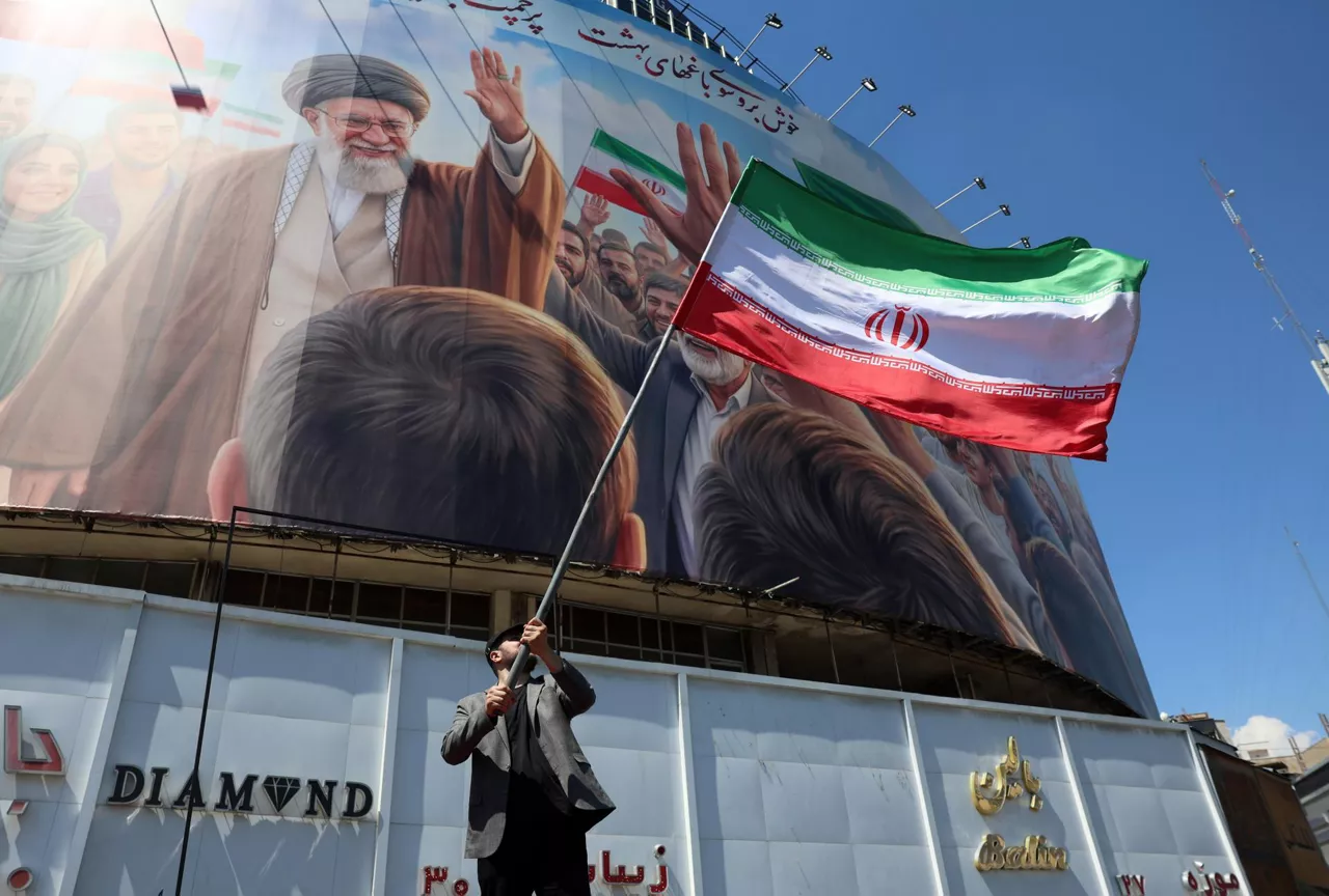 TEHRAN (IRAN(Islamic Republic Of)), 10/04/2026.- An Iranian man waves Iran's national flag in front of a large billboard showing a portrait of the late Iranian Supreme Leader Ayatollah Ali Khamenei at Valiasr Square in Tehran, Iran, 10 April 2026. Iran and the US are expected to hold negotiations in Islamabad, Pakistan, following a recently agreed ceasefire. (Teherán) EFE/EPA/ABEDIN TAHERKENAREH
